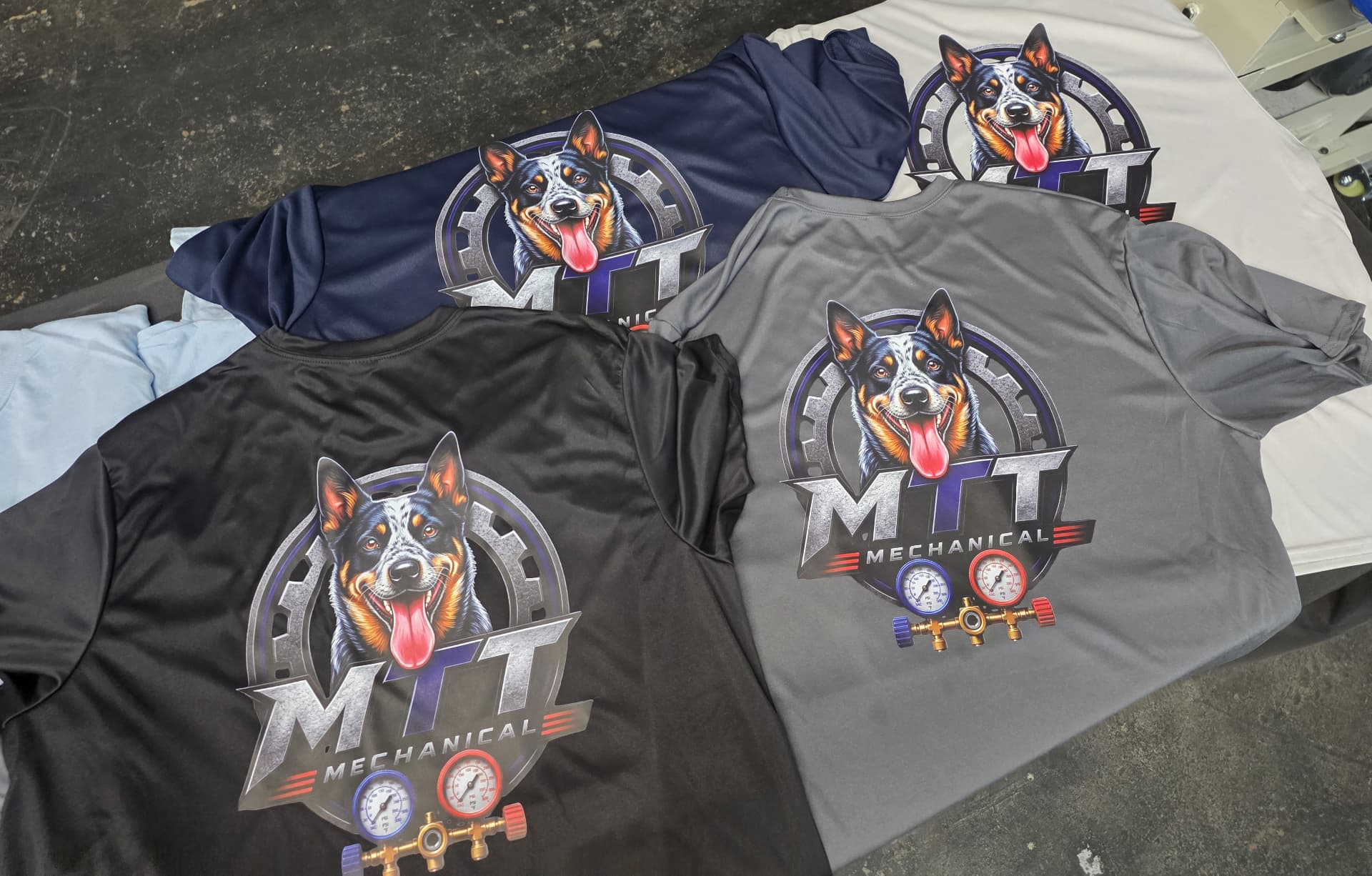 Black, navy, grey, and light blue performance shirts printed with the MTT Mechanical cattle dog logo